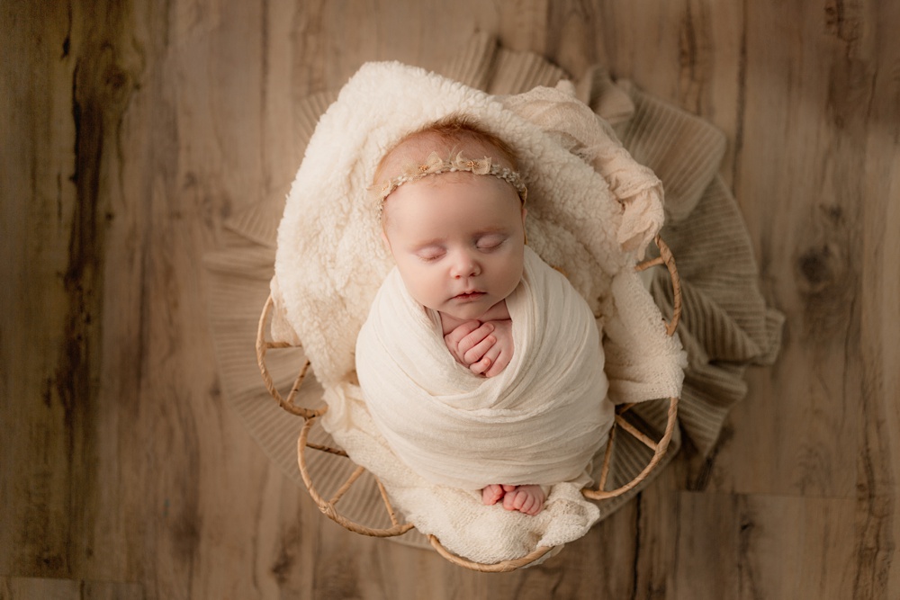 Studio newborn portrait session. Baby girl in basket with flowered headband posed in basket.