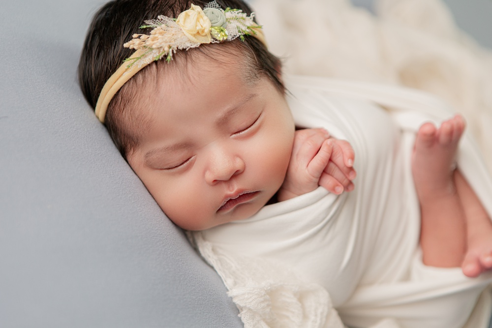 newborn baby girl in blue, white and pale yellow during her newborn portraits