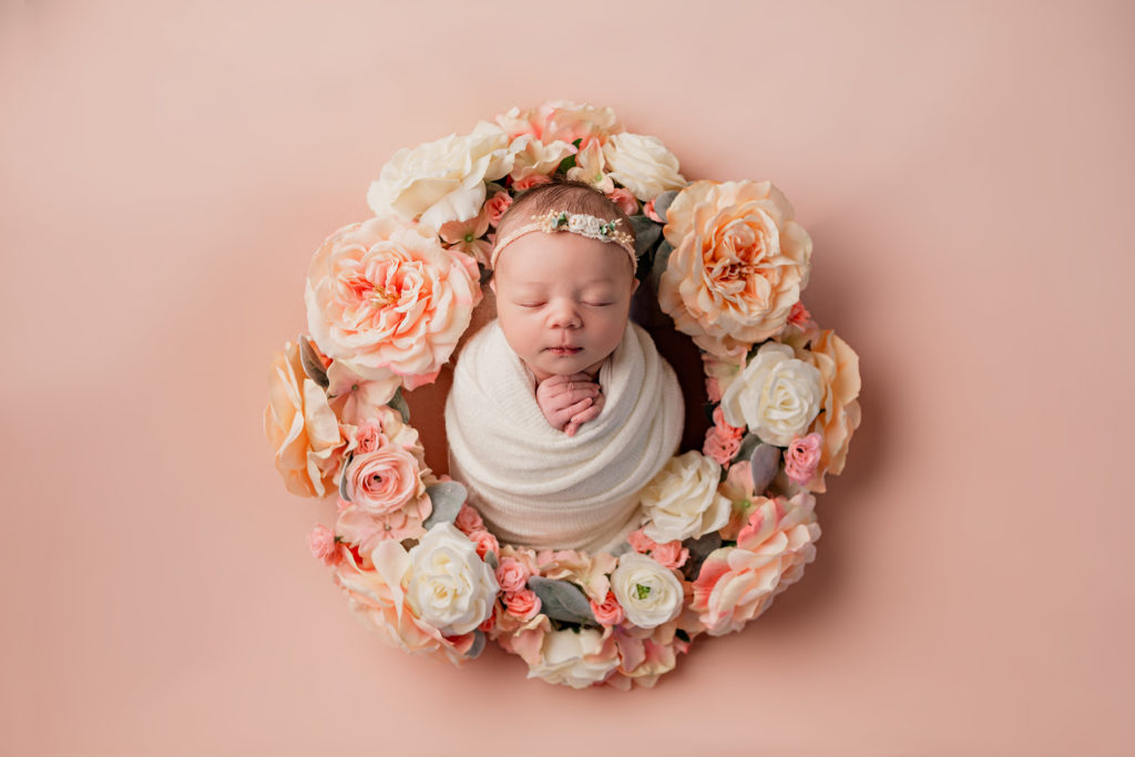 beautiful flower wreath surrounds newborn baby girl on a pink backdrop